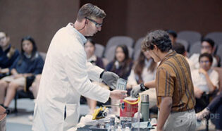 A scientist performing a small LNG demonstration in front of a student inside of a lecture hall