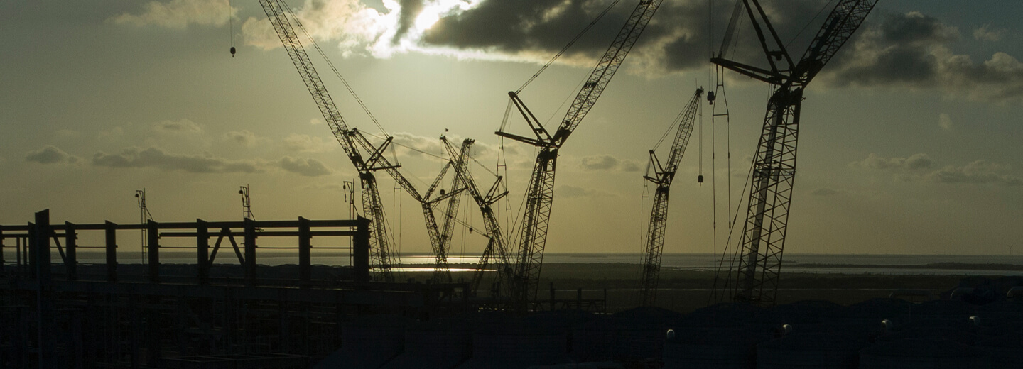 Tall cranes silhouetted against the sun at the construction of train 5 at the RGLNG terminal